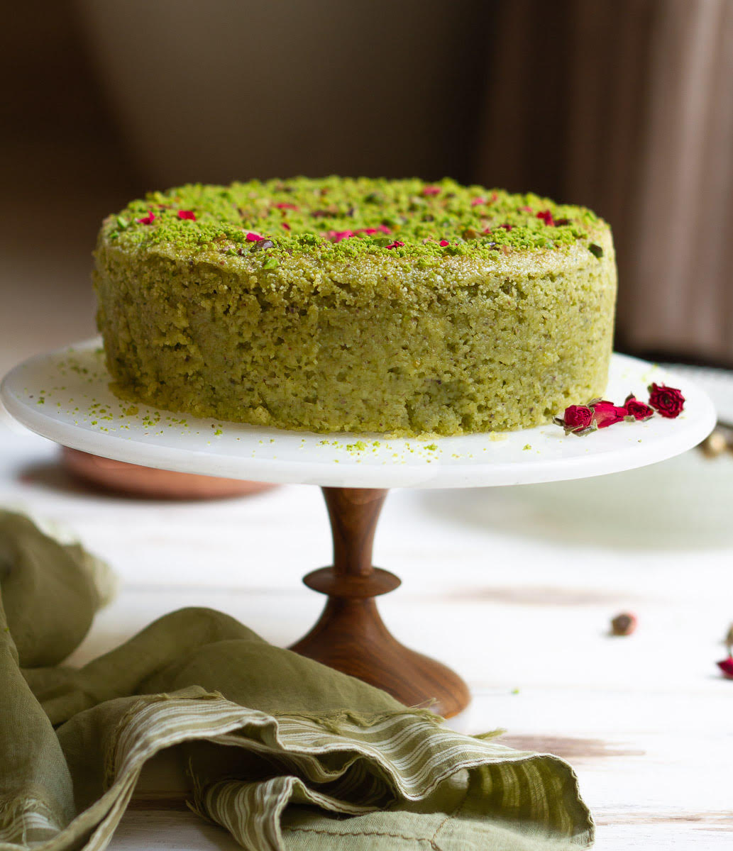 A cake with pistachios and rose petals on a cake stand.