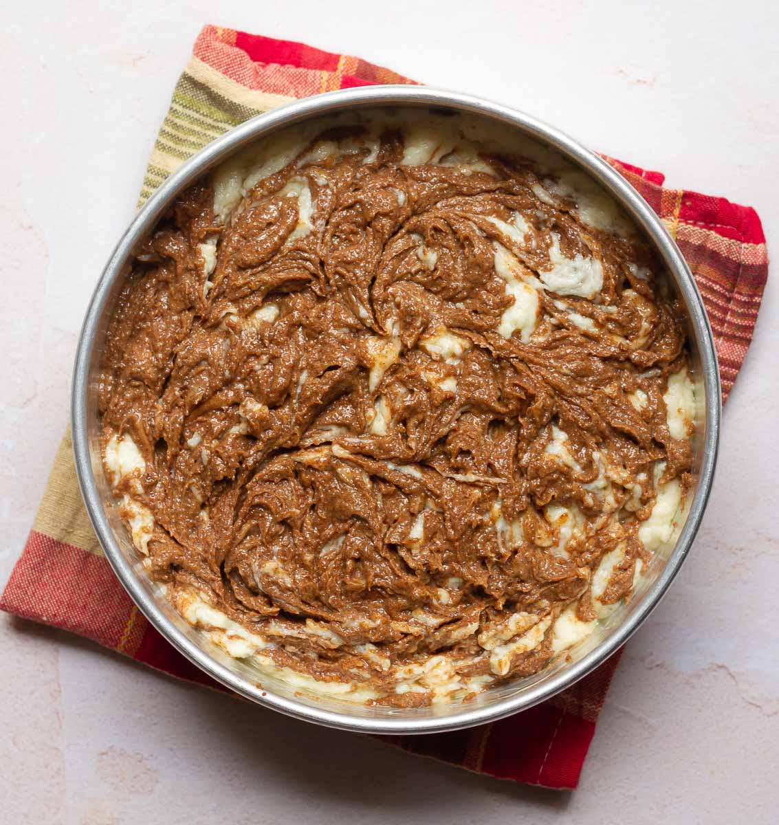 Cake batter in a cake pan with cinnamon swirls on top.