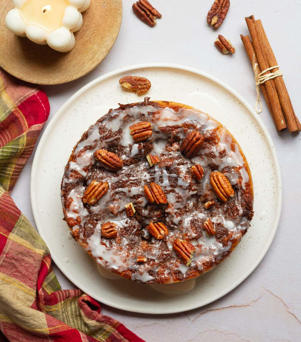Cinnamon Roll Cake on a serving platter with a candle and cinnamon sticks on the side.