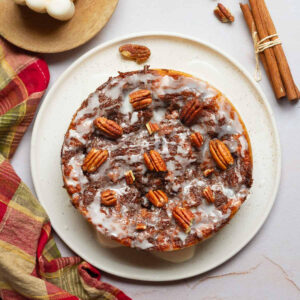 Cinnamon roll cake drizzled with glaze and topped with pecans on a plate.
