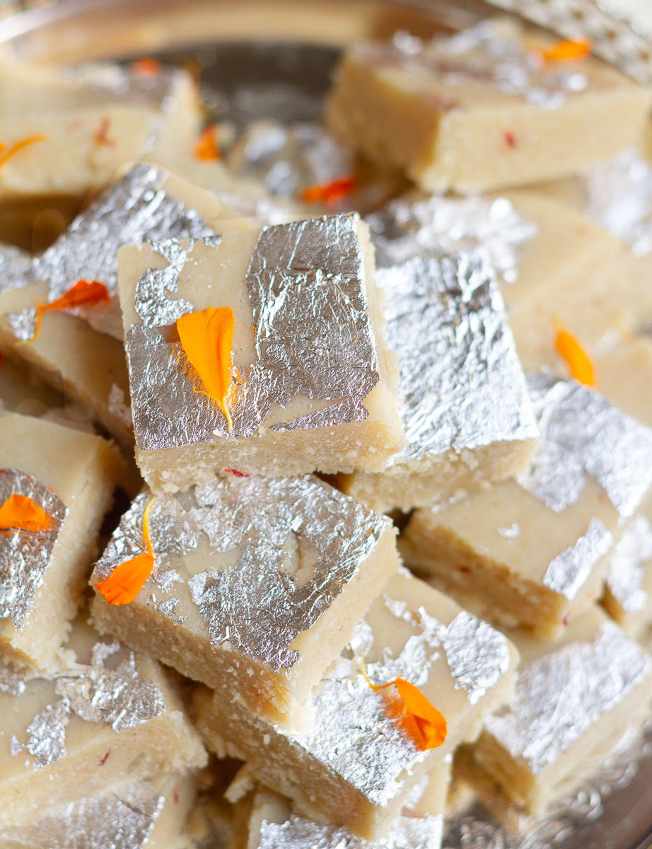 Almond burfi pieces garnished with silver leaf and marigold petals stacked up.
