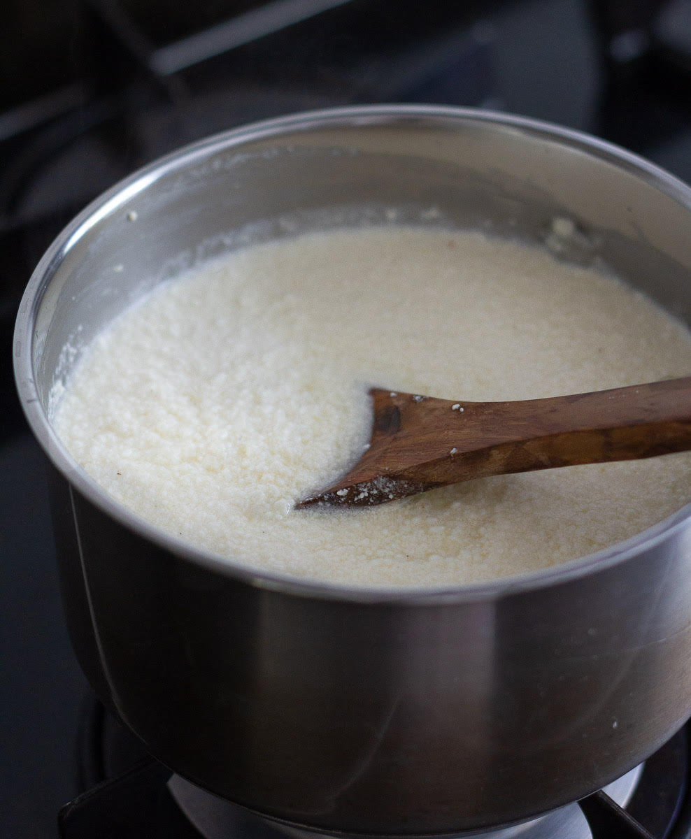 Curdled milk ad cream mixture in a saucepan with a wooden spoon.