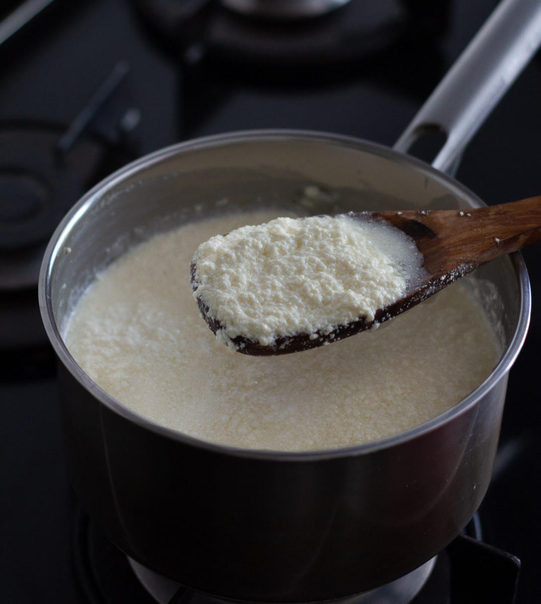 Fully curdled milk and cream mixture on a wooden spoon on a saucepan.