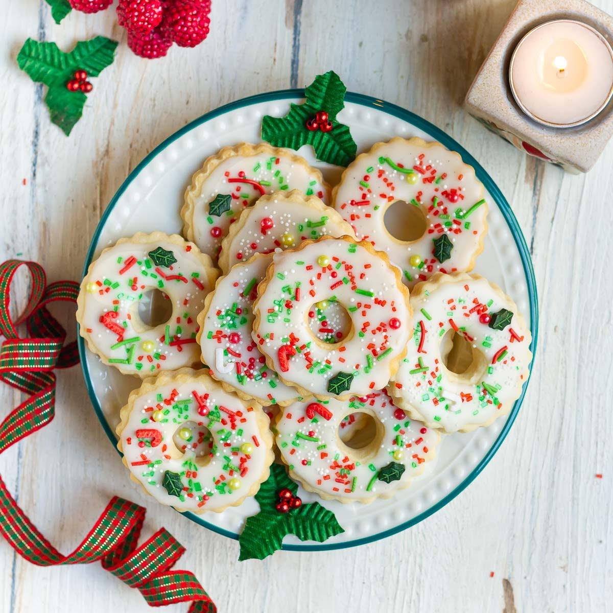 decorated christmas wreath cookies on a plate with christmas decor around.