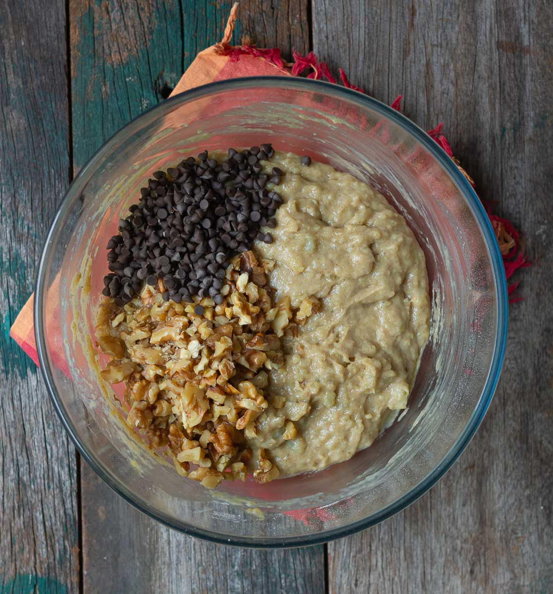 Walnuts and chocolate chips on top of a cake batter in a mixing bowl.