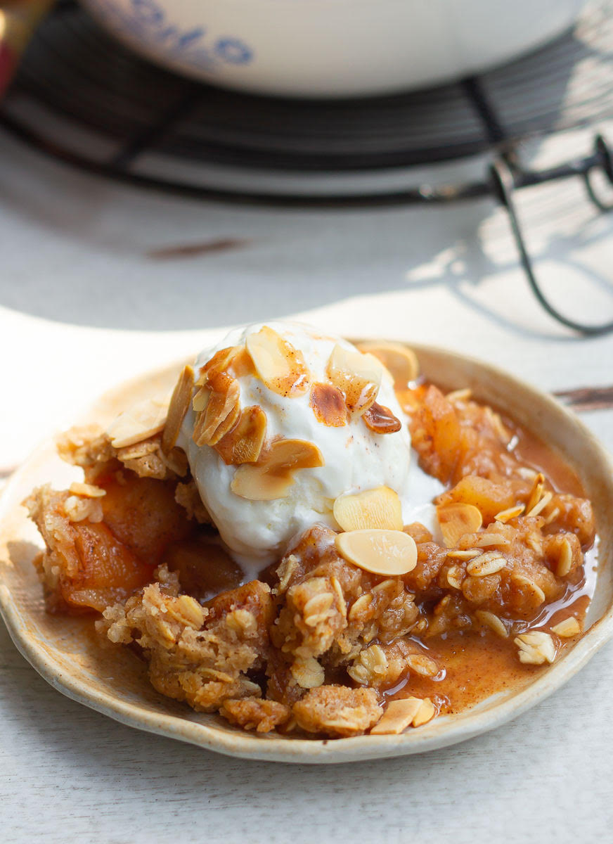 Bowl of apple crisp with ice cream and almond flakes on top.