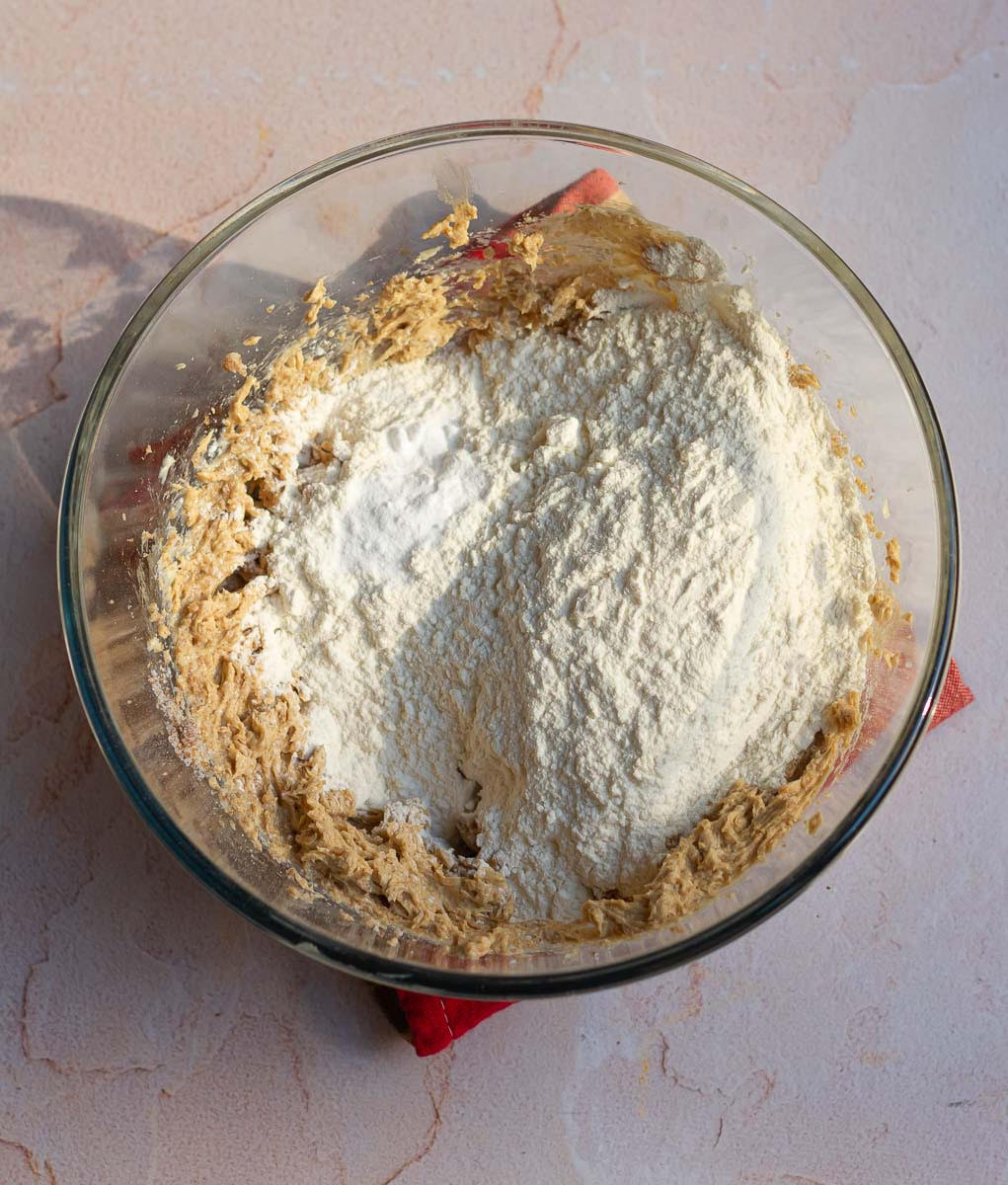 Flour and baking soda on top of butter-sugar mixture in a mixing bowl.
