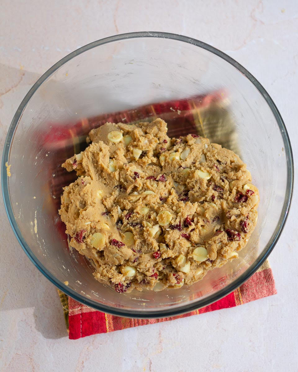 Cookie dough with white chocolate, macadamia nuts, and cranberries in a mixing bowl.