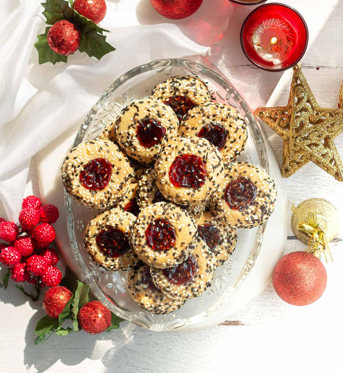 Jam thumbprint cookies on a glass platter with christmas decorations around.