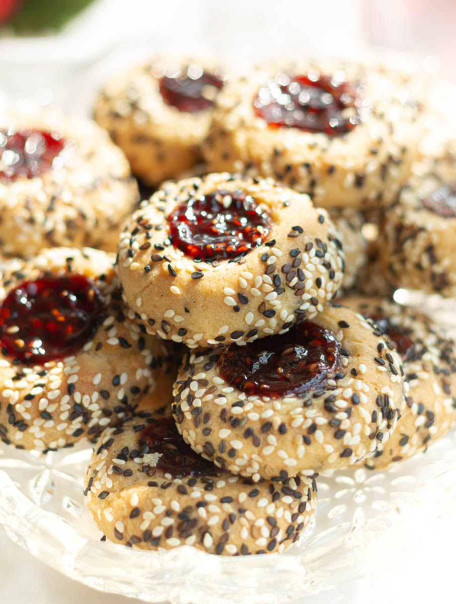 Cookies coated with black and sesame seeds and with jam in the center on a tray.