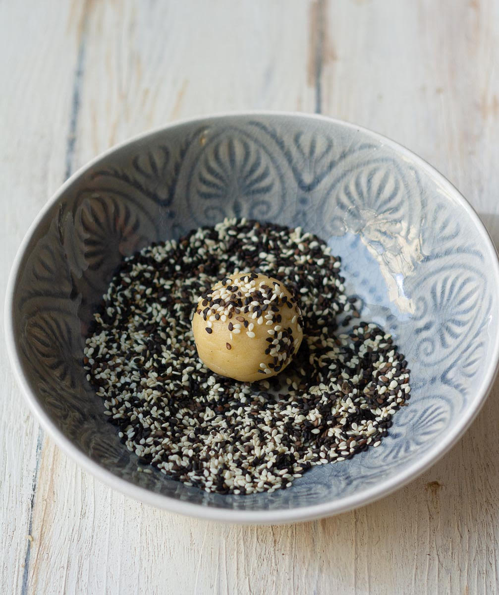 Dough ball in a bowl of black and white sesame seeds.