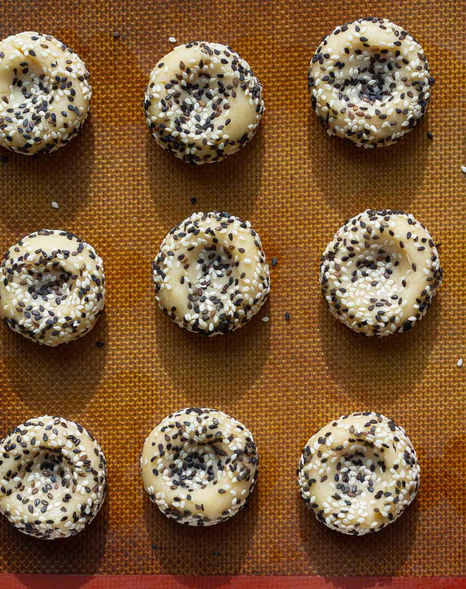 Cookie dough balls coated in sesame seeds with indentation on a tray.