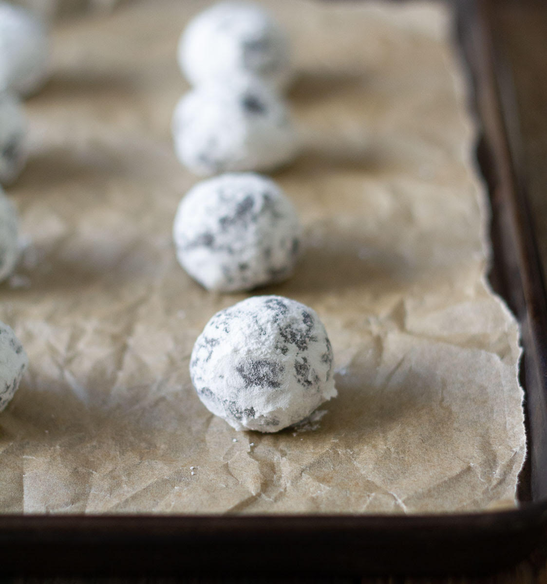 Cookie dough balls coated with icing sugar on parchment paper.