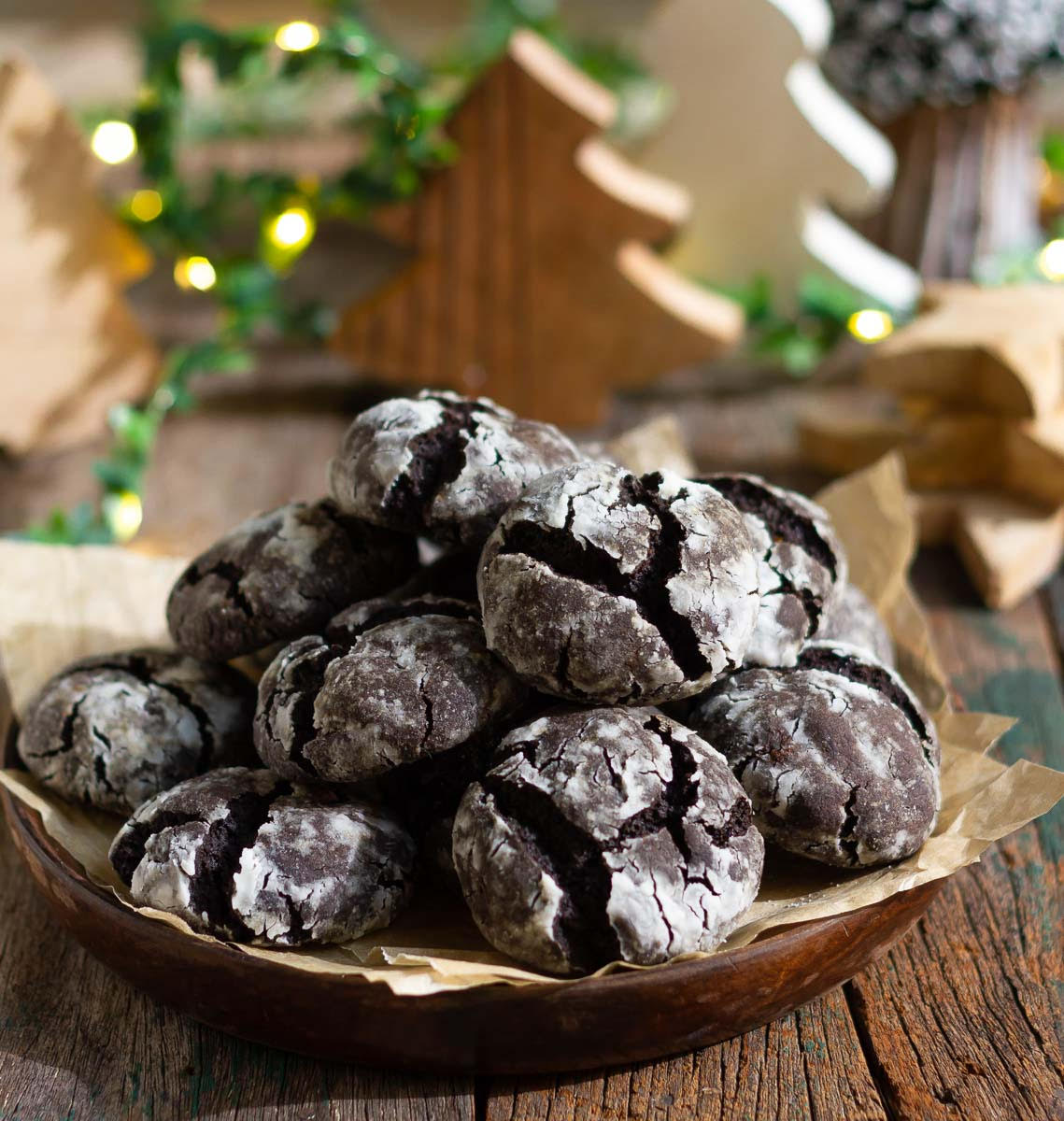 Chocolate crinkle cookies in a wooden plate, surrounded by christmas decor.