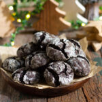 Chocolate crinkle cookies on a parchment paper lined wooden platter.