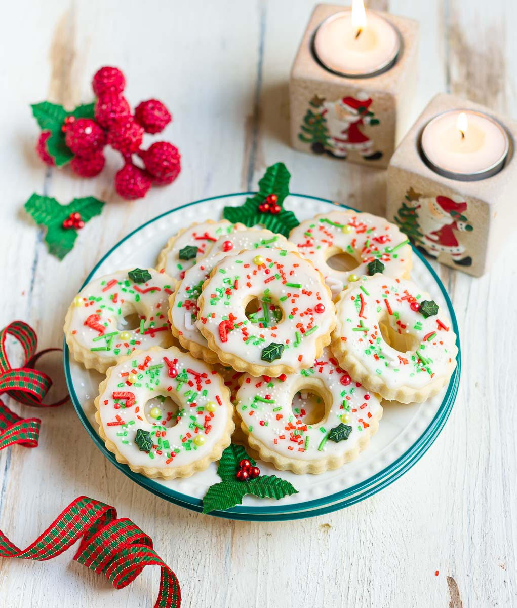 Decorated christmas cookies on a plate with christmas decorations around.