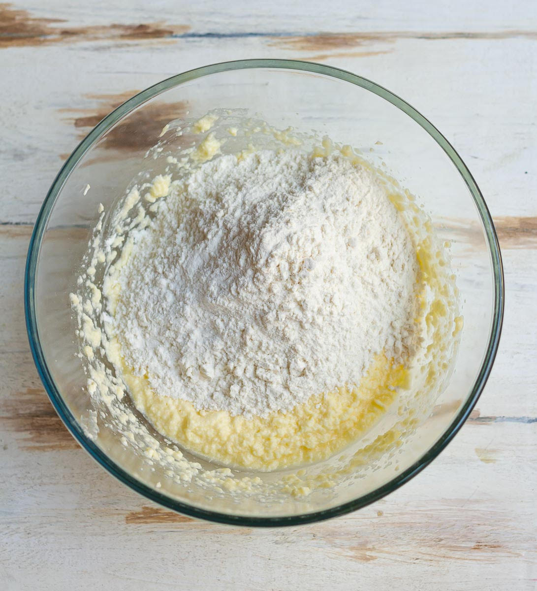 Flour on top of butter-sugar mixture in a mixing bowl.