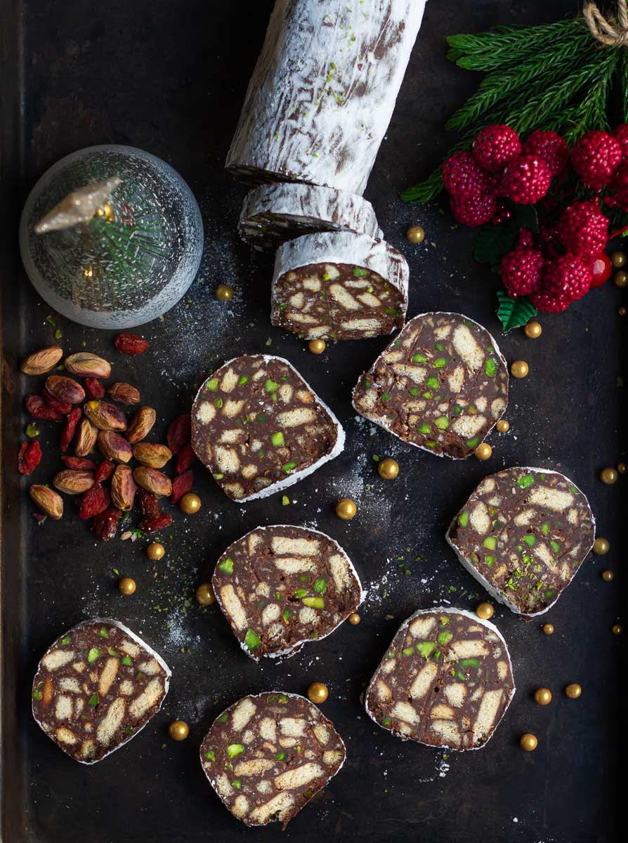 Slices of chocolate salami with nuts on the side on a black tray.