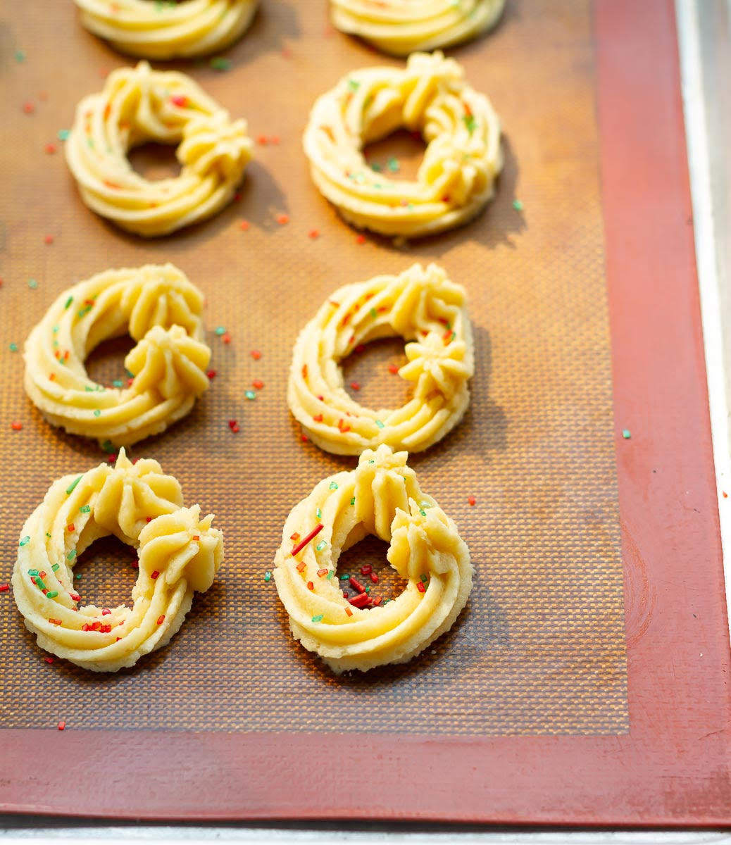 Piped cookie dough with sprinkles on a silpat sheet.
