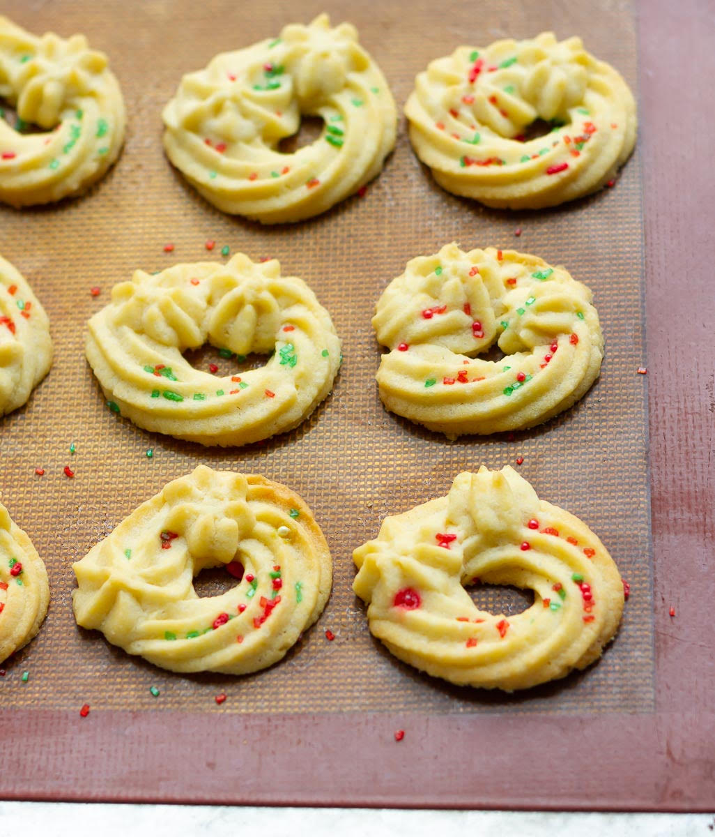 Baked spritz cookies with red and green sprinkles on a silpat sheet.