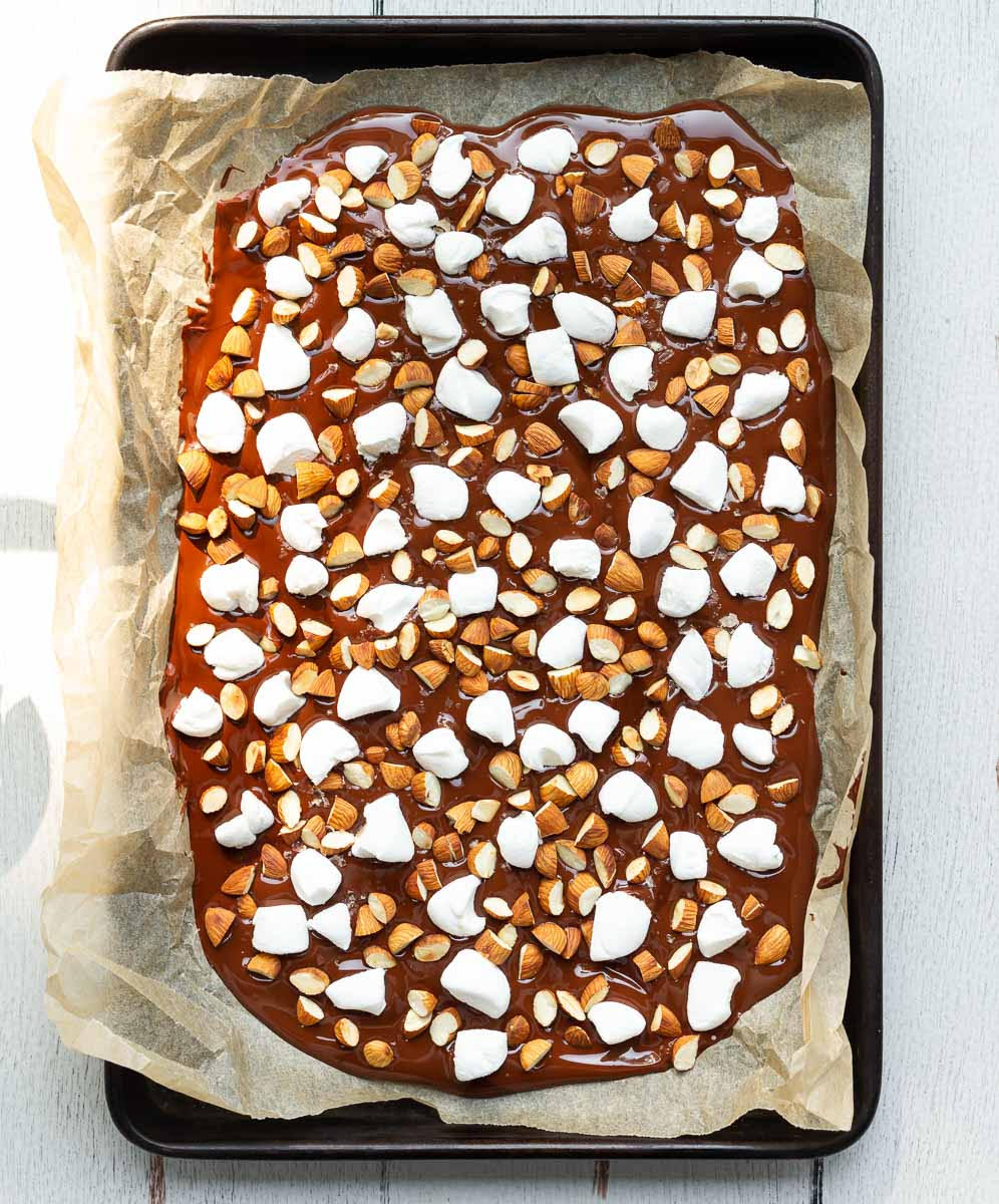 Almonds and marshmallows on top of melted chocolate on parchment paper.