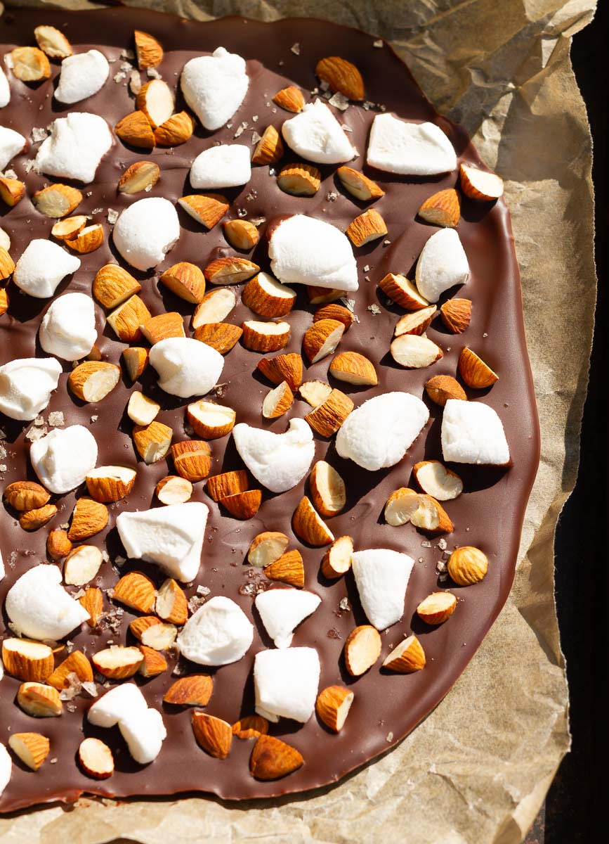 Melted chocolate with almonds and marshmallows on parchment paper.