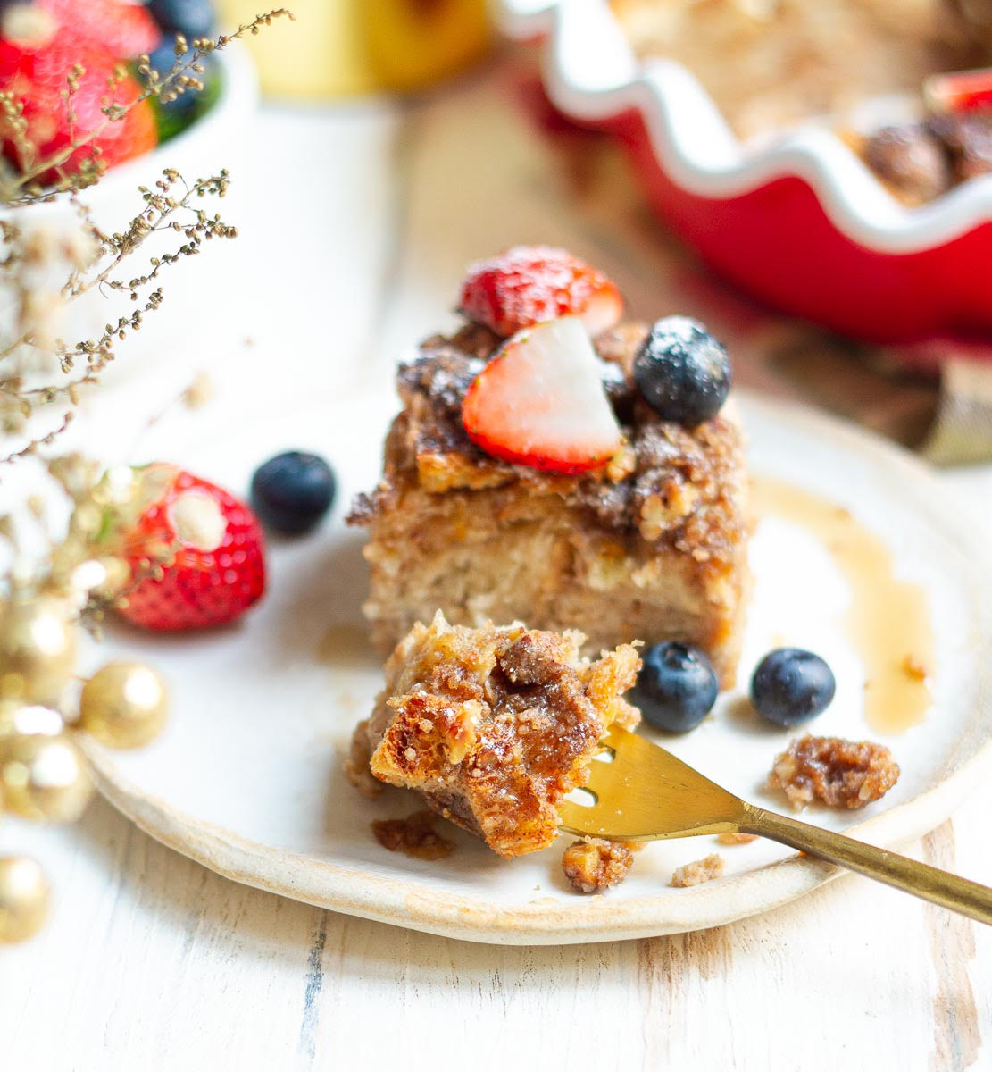 A slice of casserole with berries and maple syrup and a fork on a small plate.