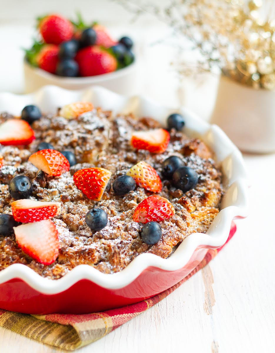 Baked French toast casserole topped with sugar, blueberries, and strawberries.