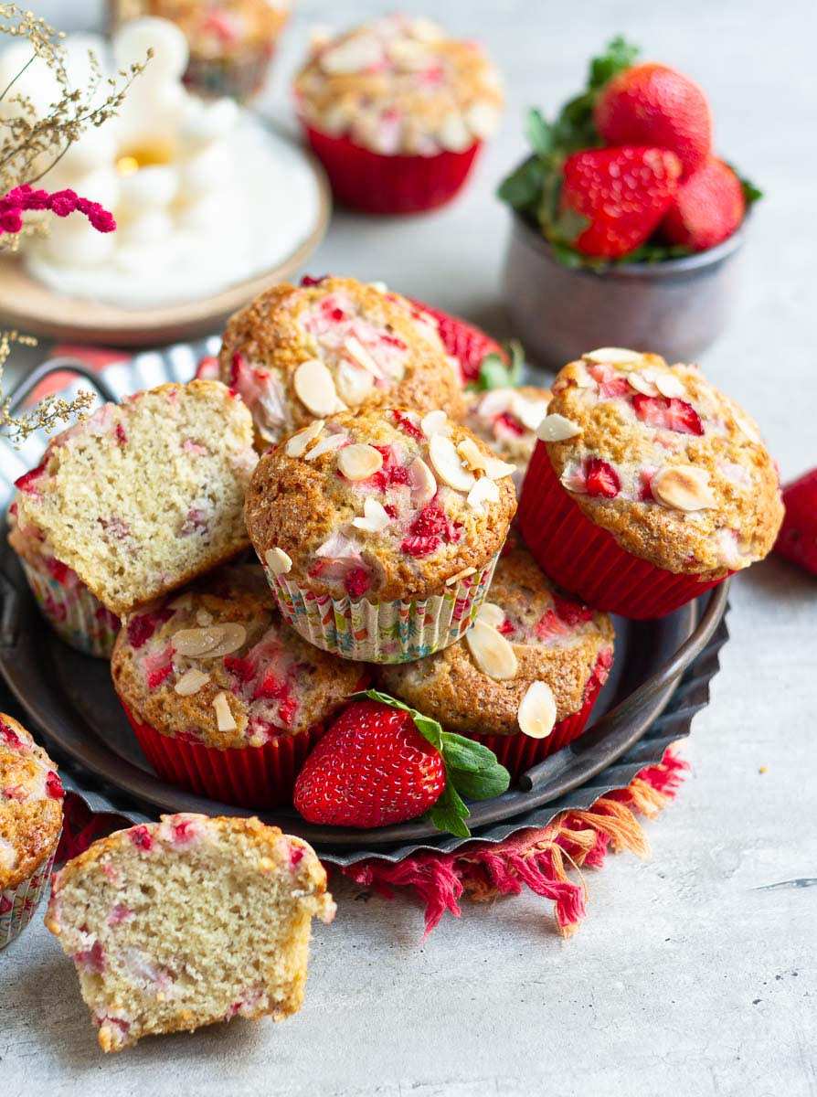Strawberry Banana Muffins stacked in a metal tray with 2 halves of a cut muffin to show the texture.