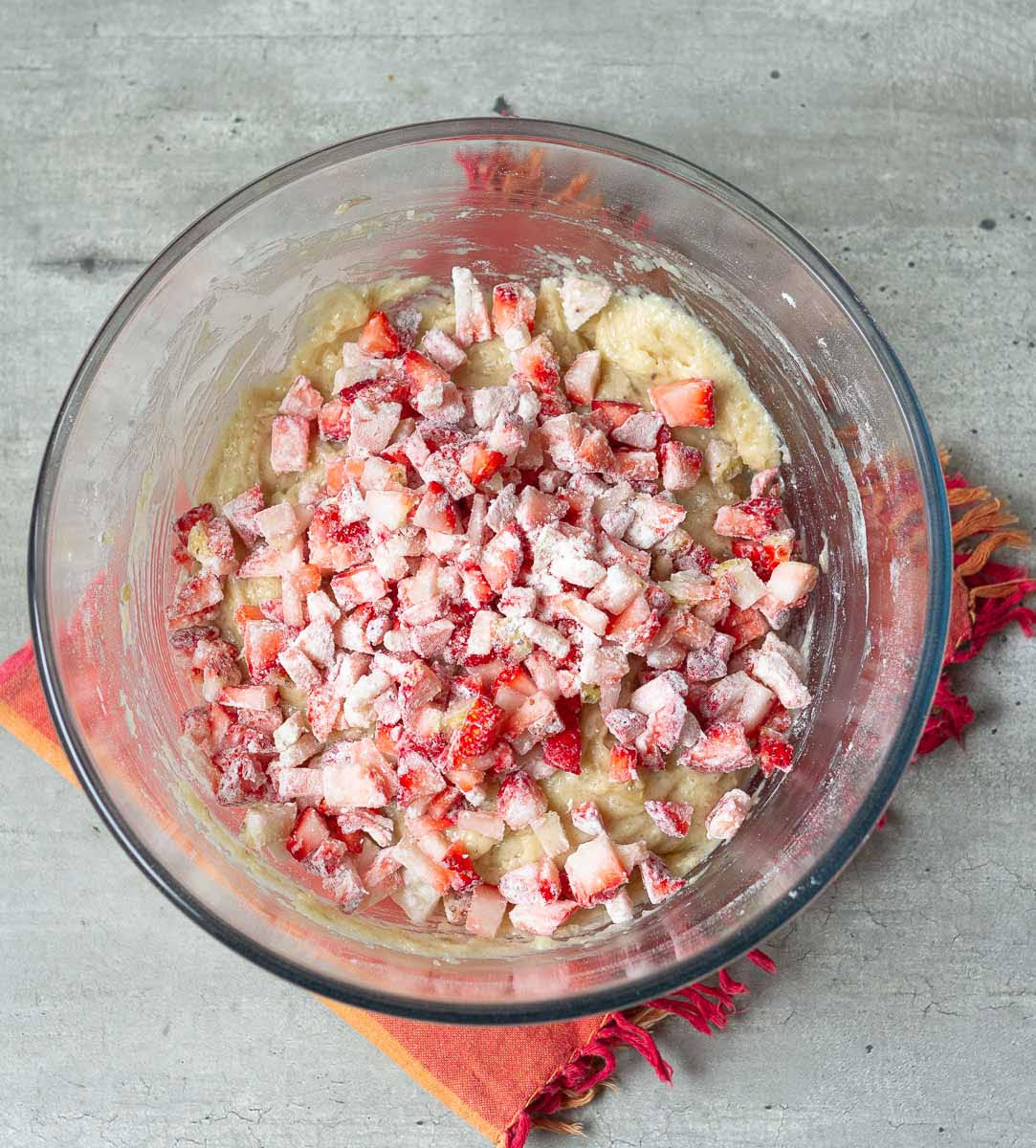 Chopped strawberries tossed in flour on top of muffin batter in a mixing bowl.