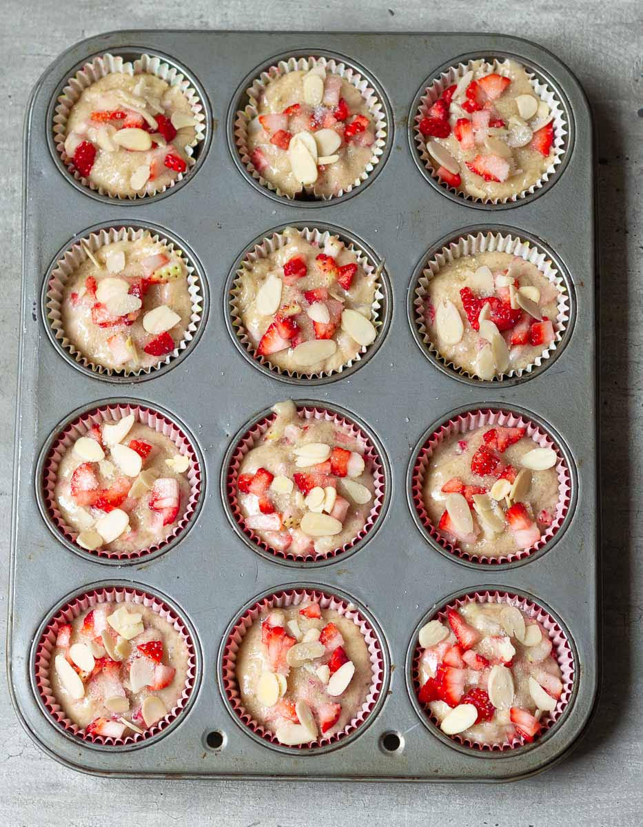 muffin batter topped with almond flakes in a muffin tray.