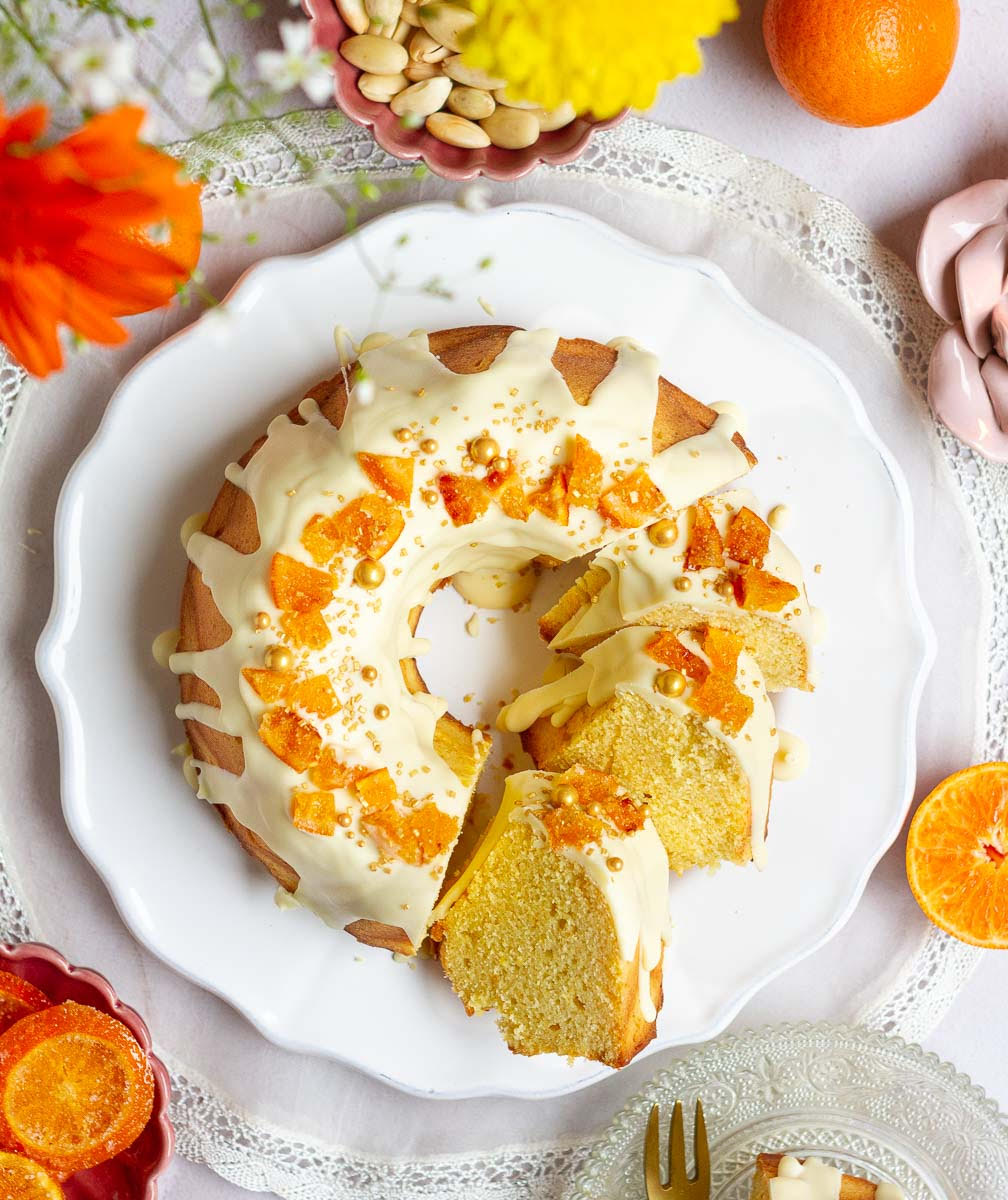 Sliced cake with white chocolate glaze and candied oranges on a platter.