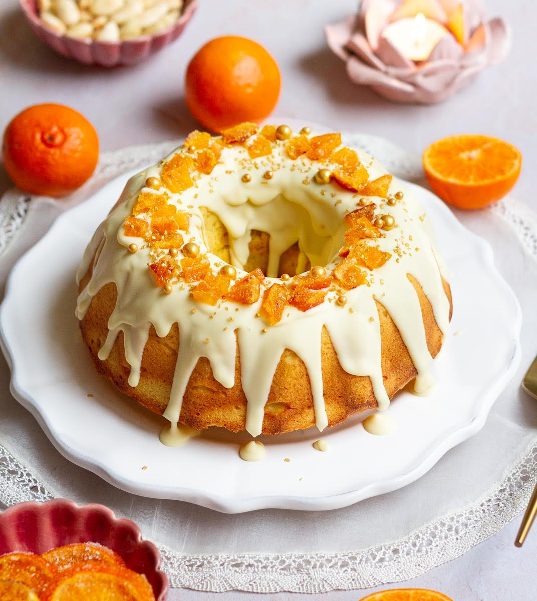A bundt cake with white glaze and candied oranges on a serving platter.