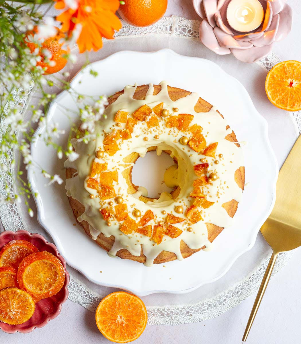 Orange bundt cake with white chocolate frosting and candied oranges on top.