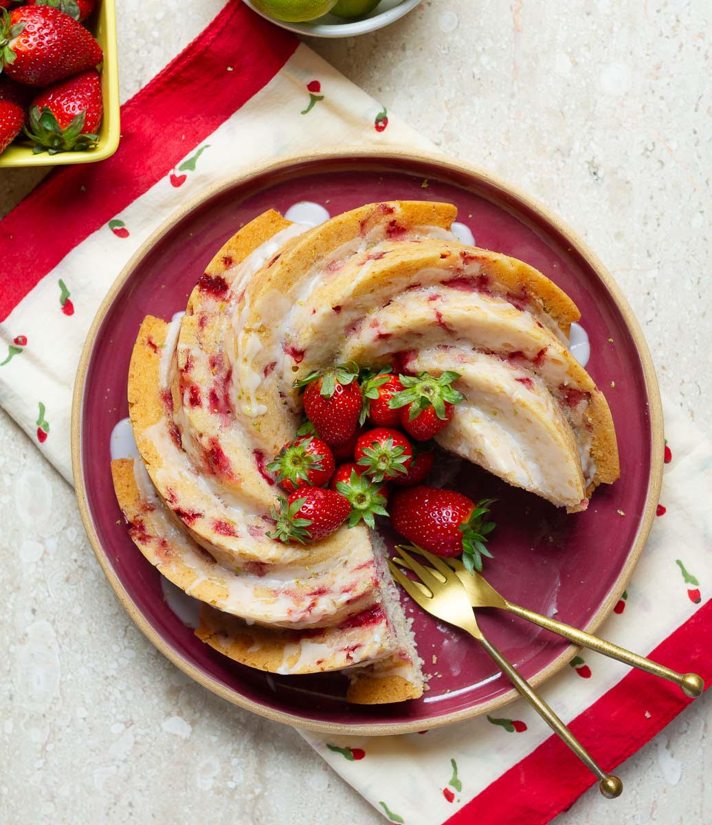 cake with fresh strawberries on a platter with 2 forks and a slice taken out.