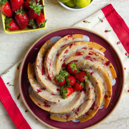 Strawberry Bundt Cake on a red platter with strawberries on the side.