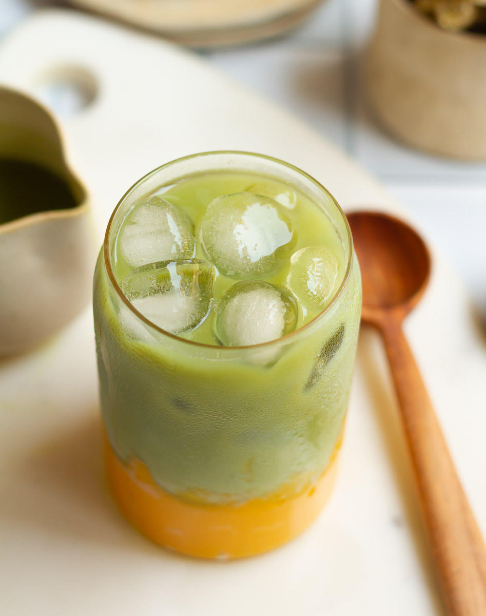 Mango Matcha Latte in a glass with a wooden spoon.