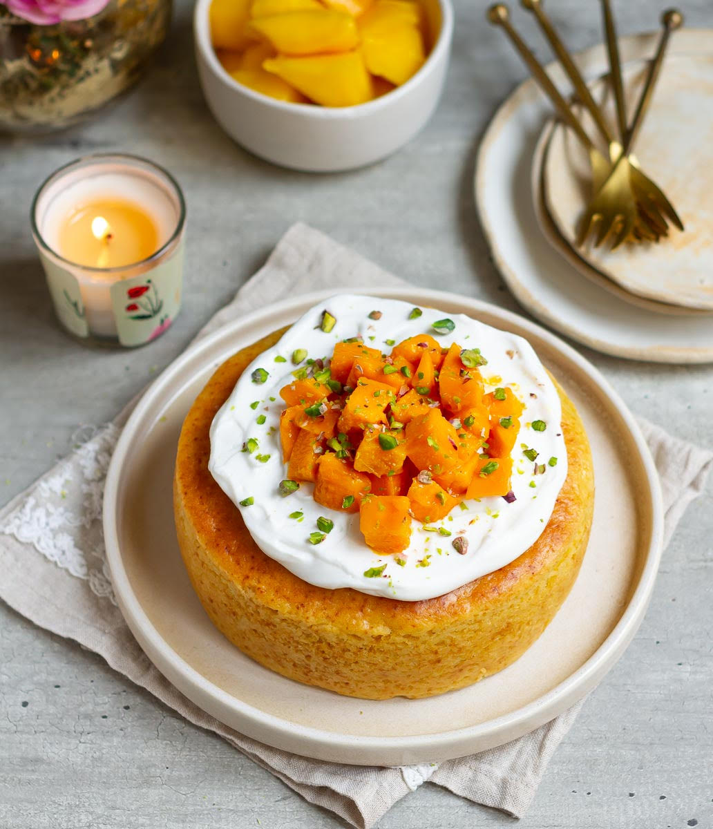 Decorated mango cake on a platter with ingredients in the background.