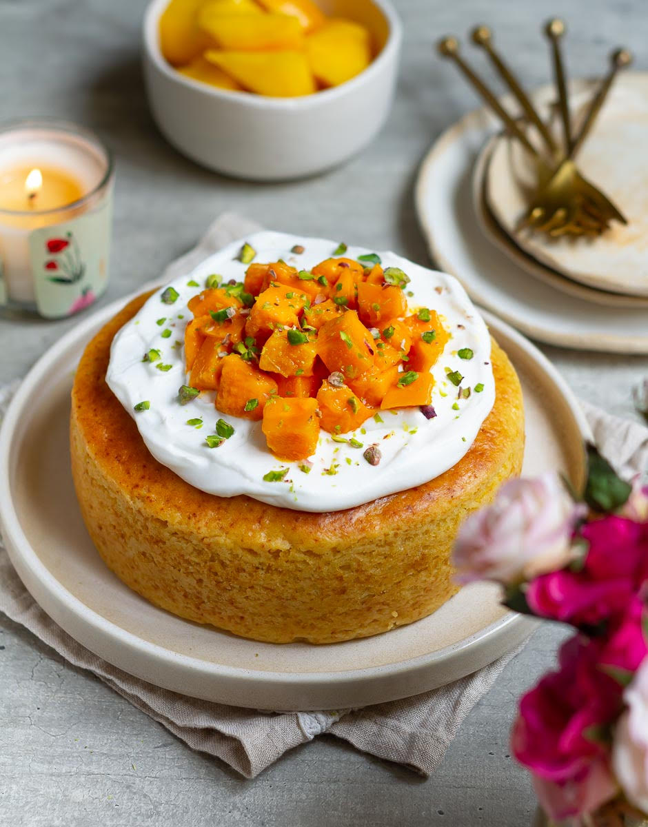 mango cake topped with whipped cream and mangoes on a platter.