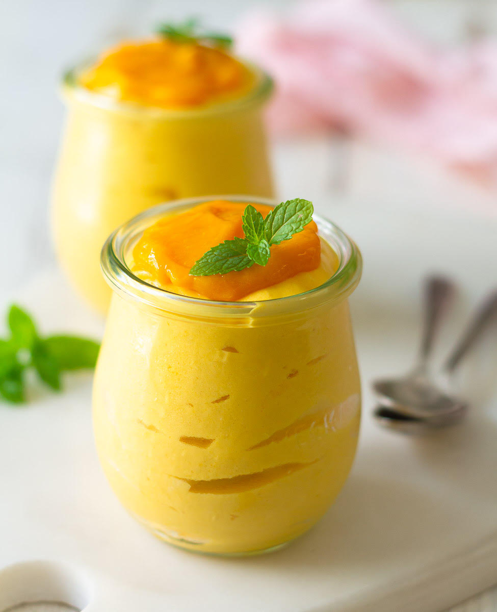 Mango mousse in 2 jars topped with mango puree and mint leaves.