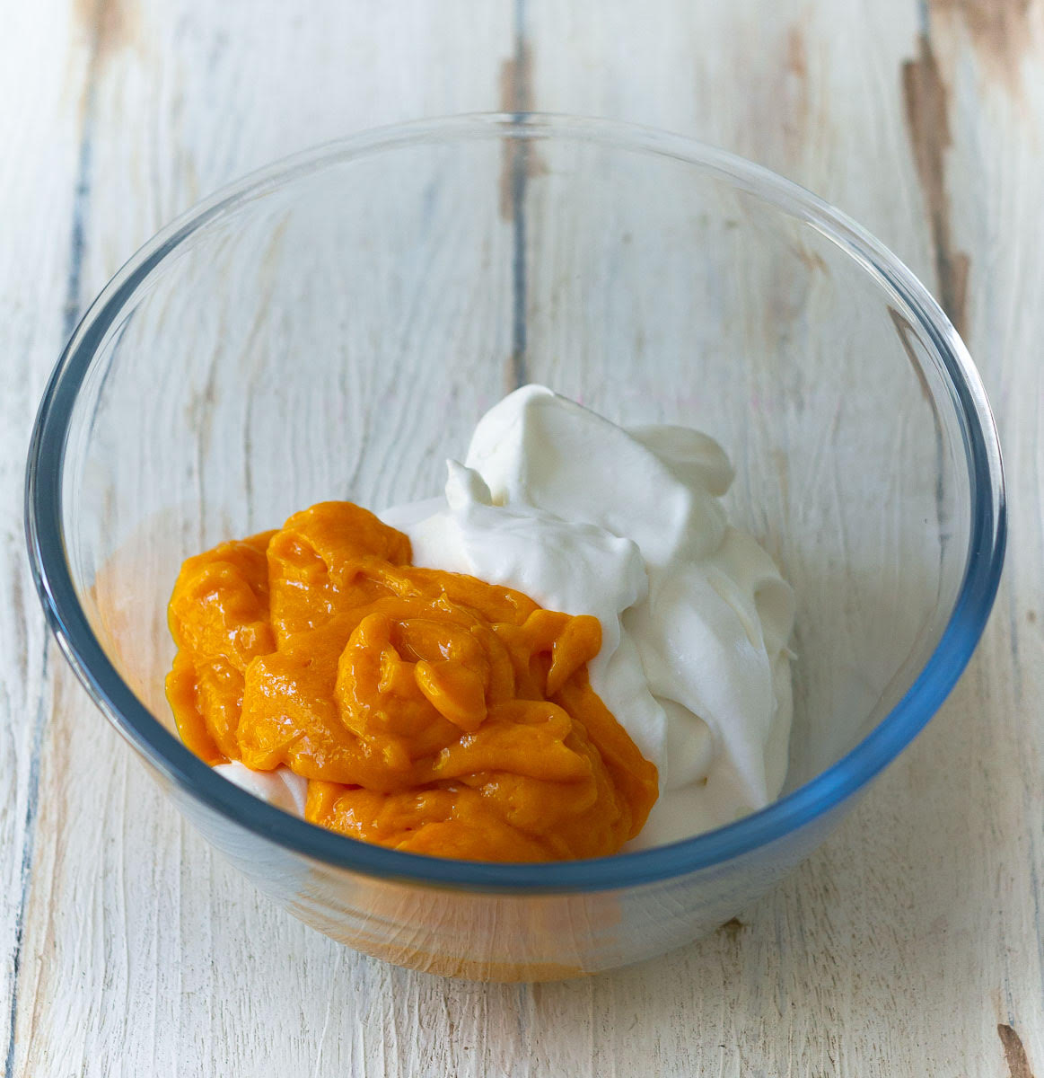 Folding the mango puree into the whipped cream in a bowl.