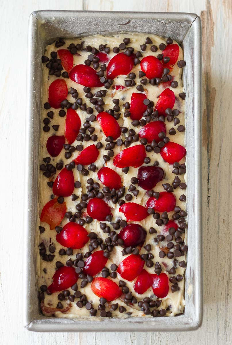 Cake batter in a loaf pan topped with cherries and chocolate chips.