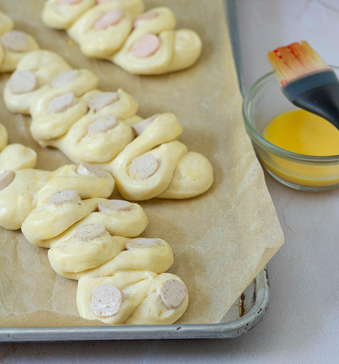 Shaped breads on a parchment paper lined baking tray with egg in a bowl.