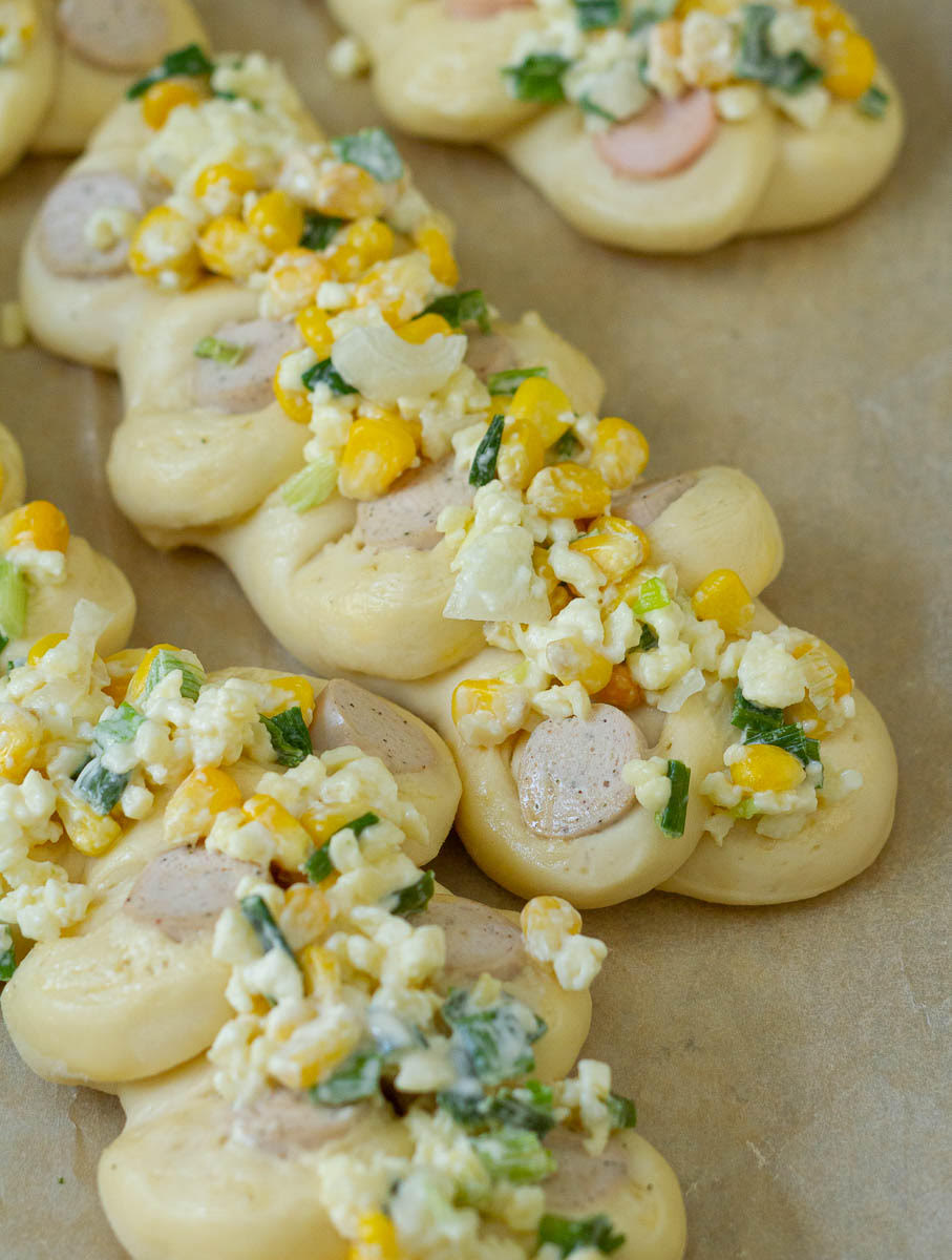 Bread rolls topped with corn mixture on parchment paper.