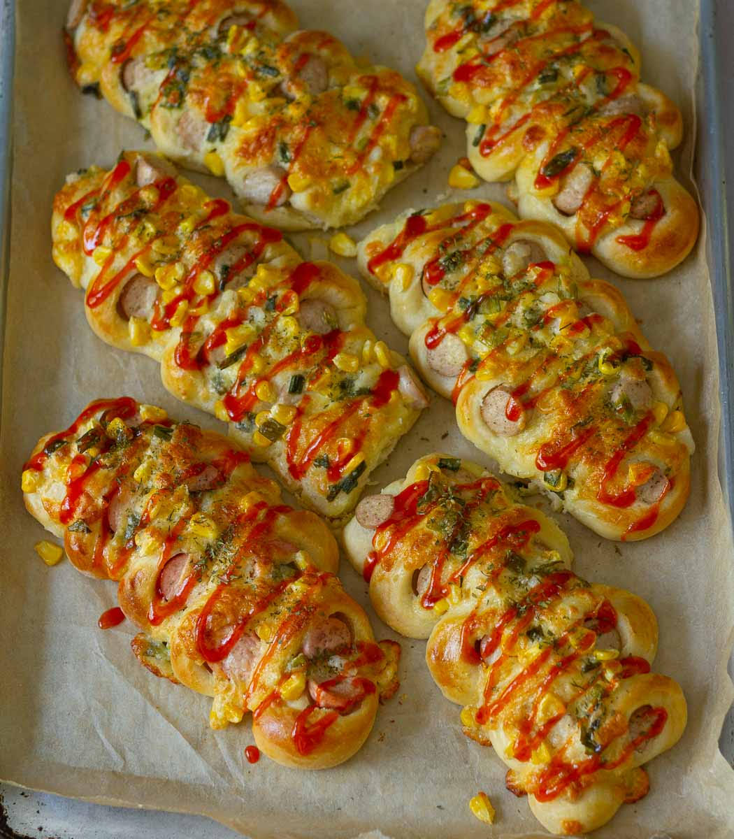 6 Korean sausage rolls drizzled with Sriracha sauce on parchment paper.
