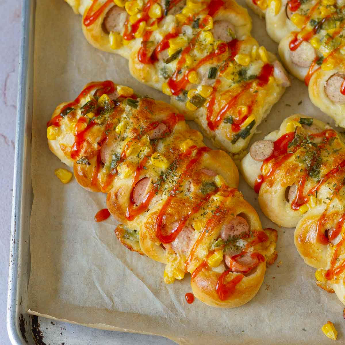 Korean sausage breads on a baking tray lined with parchment paper.