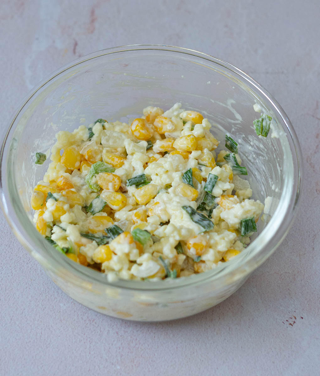 Corn, mayonnaise, green onions and cheese mixture in a small bowl.