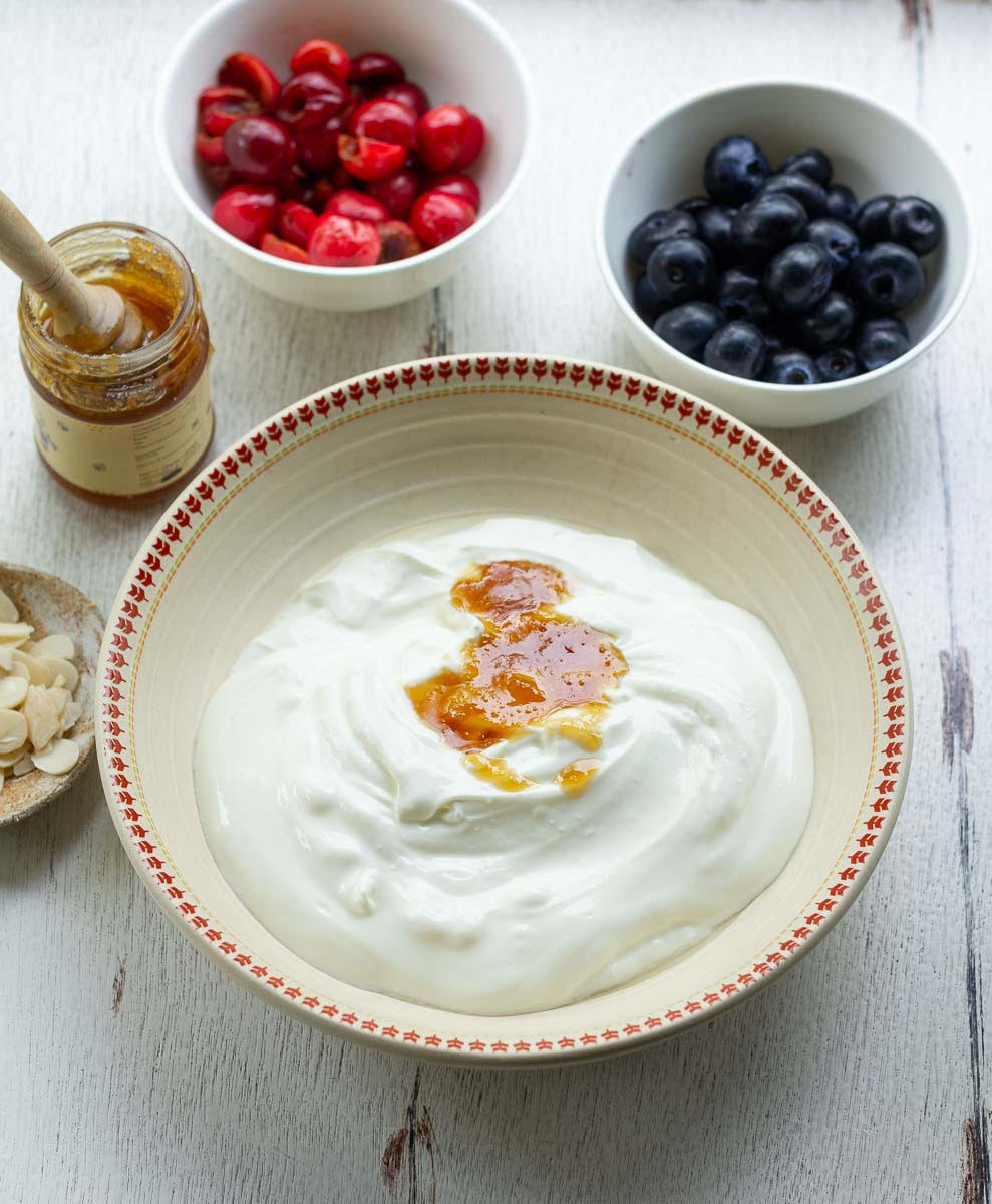 Whisking honey and Greek yogurt in a bowl with ingredients in the background.