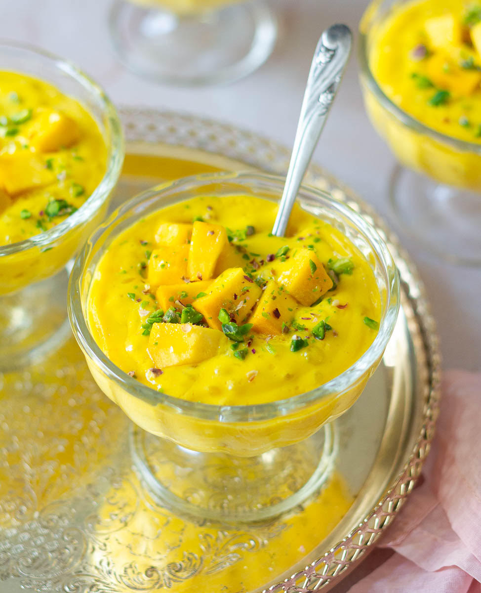 Mango sago topped with mangoes and pistachios in a dessert cup with a spoon in it.
