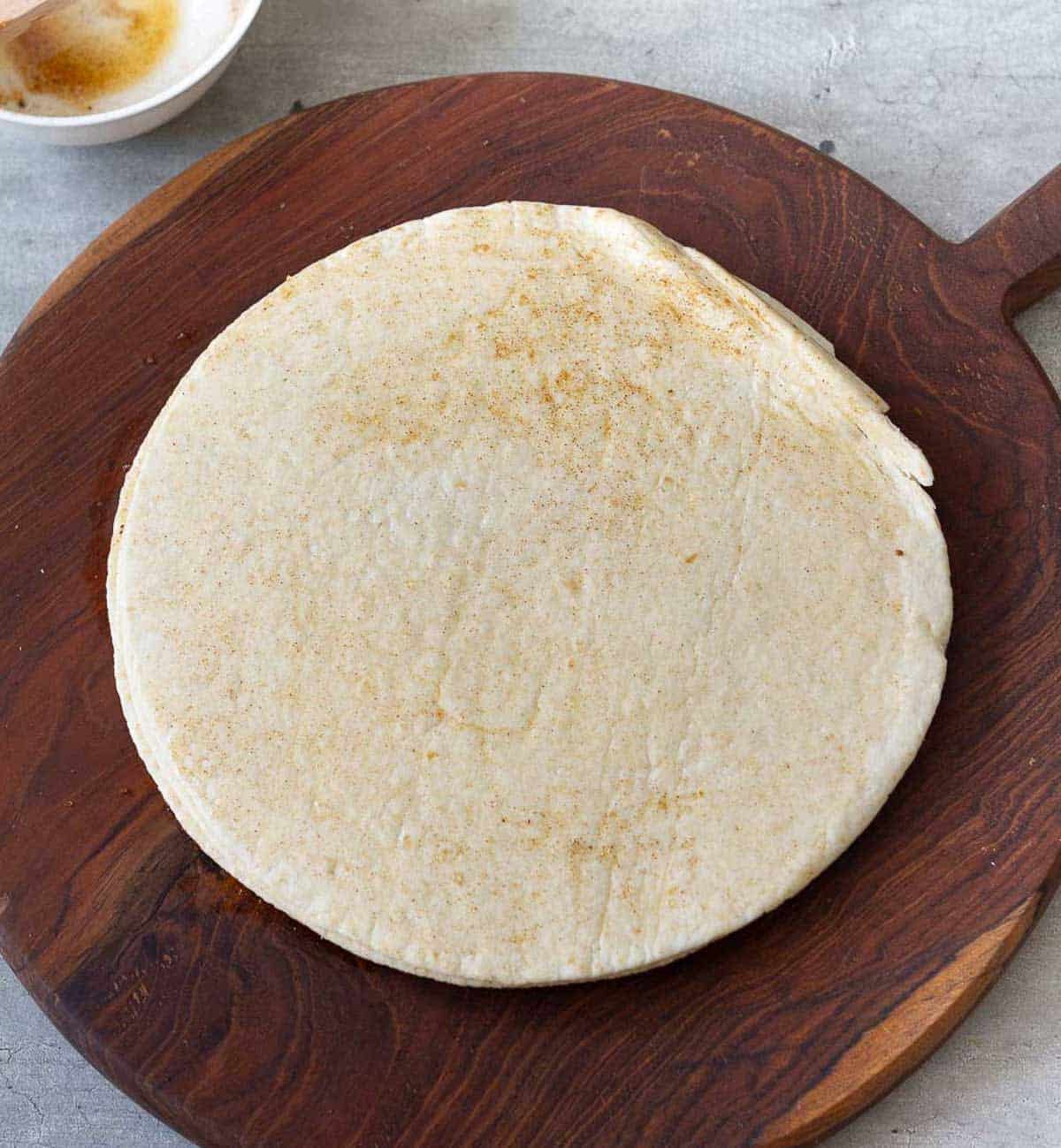 A stack of tortillas brushed with the seasoning on a wooden board.